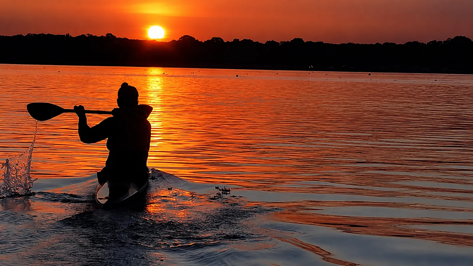 Kayaker paddling into the sunset on calm water